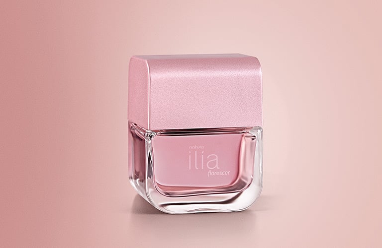 Foto de un frasco de perfume Ilía de Natura, de vidrio transparente con líquido rosa y tapa rosa, sobre un fondo degradado en tonos rosados.